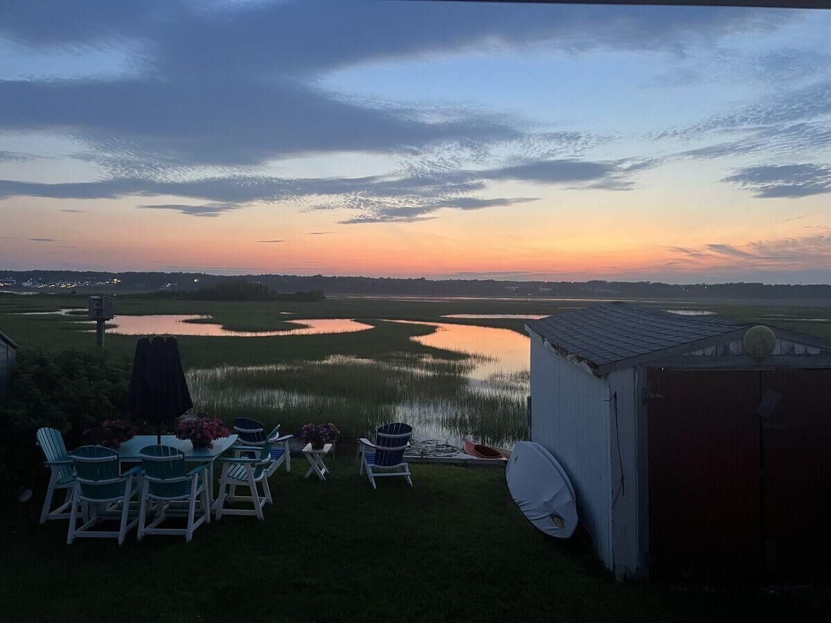 Un patio con mobiliario exterior, un cobertizo pequeño y vistas a un lago al atardecer.