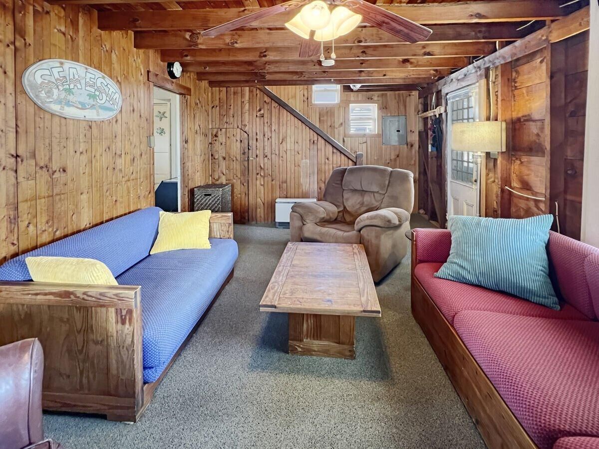 A cozy cabin interior with a blue sofa, a red sofa, a wooden coffee table, and a ceiling fan.