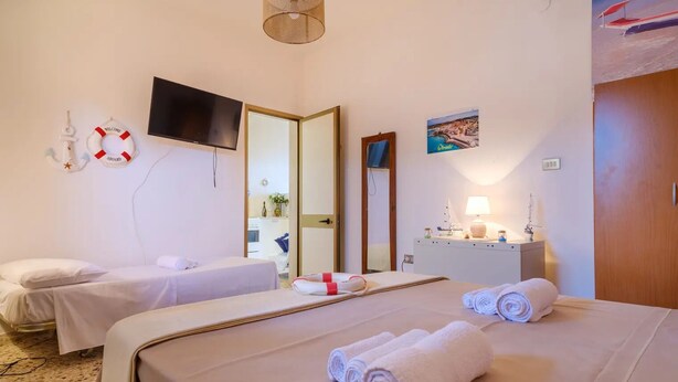 A hotel room with two beds, a TV, a mirror, a desk with a lamp, and a view of the sea. - Alla Rosa Dei Venti Sud Wind House (Torre Specchia Ruggeri)