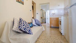 A hotel room with a sofa, patterned cushions, a clock, a kitchen area with a stove and refrigerator, and a door leading to another room. - Alla Rosa Dei Venti Sud Wind House (Torre Specchia Ruggeri)