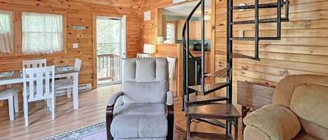 A cozy cabin interior with a dining area, a comfortable seating area, and a spiral staircase.