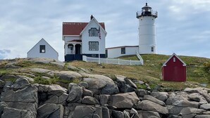 A lighthouse with a white tower and a red building nearby. - Beach Daze Cottage (York Beach)
