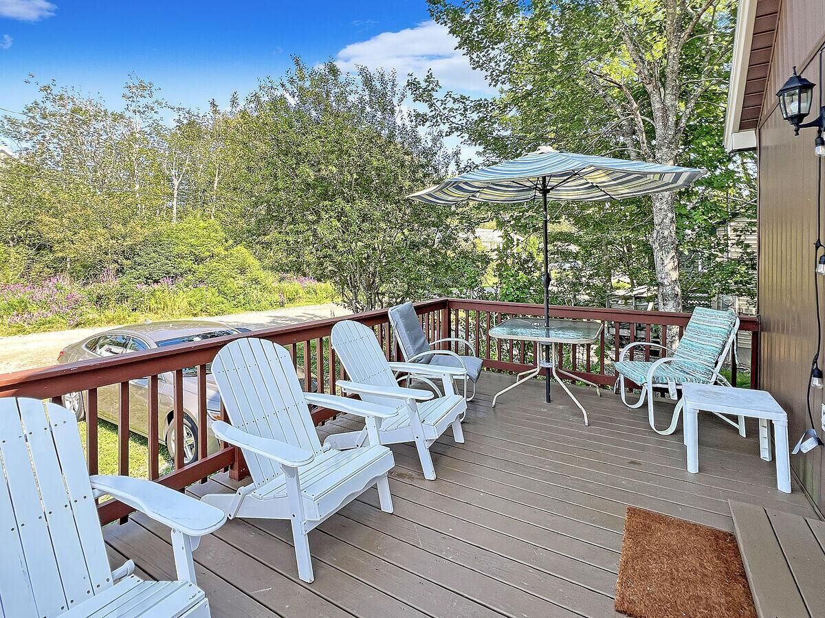 A wooden deck with white Adirondack chairs, a glass table, and a striped umbrella.