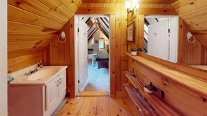 A wooden interior with a bathroom featuring a sink and cabinets, a mirror, and a bench. - Plymouth Ski Farm (Bridgewater Corners)