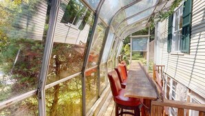 Een overdekte eethoek buiten, met een tafel en stoelen, omgeven door glazen wanden en houten leuningen.