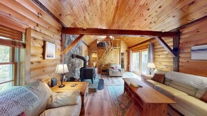 Een chaletinterieur met een stenen openhaard, houten meubels en een trap naar een verdieping.