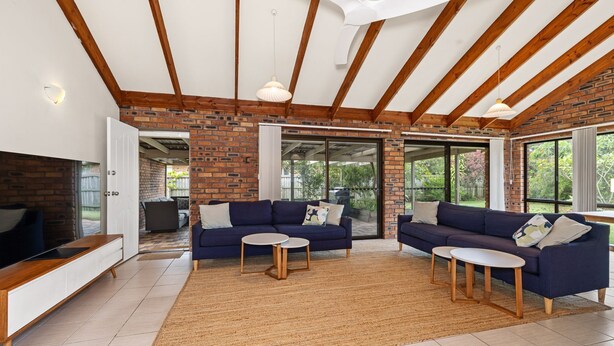 A spacious living area with a brick wall, wooden beams, and large windows.