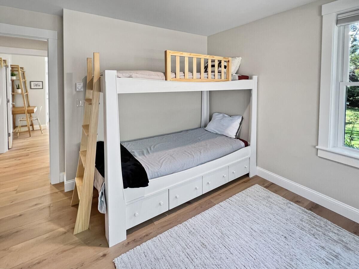 A bunk bed with a wooden headboard, a white mattress, and a white wall.