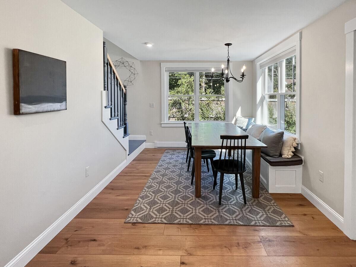 A dining area with a wooden table and chairs, a patterned rug, a bench with cushions, and a staircase leading to another level.