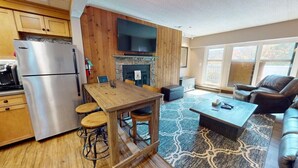 A modern kitchen with a stainless steel refrigerator, wooden cabinets, a built-in TV, and a stone fireplace. - Mt Green 1-f05 (Killington)