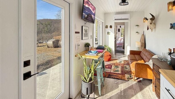 A well-lit room with a dining area, a sofa, and a TV mounted on the wall. - Zen Box Farm (Bomoseen)