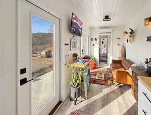 A well-lit room with a dining area, a sofa, and a TV mounted on the wall. - Zen Box Farm (Bomoseen)