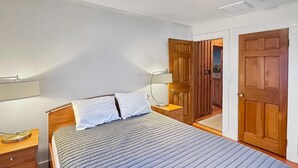 A bedroom with a bed, wooden wardrobe, and a nightstand with a lamp. - Raven's Nest (Ogunquit)