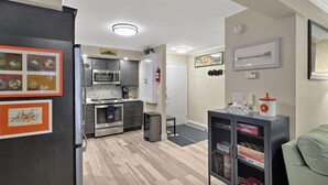 A modern kitchen with stainless steel appliances, a built-in oven, and a microwave. There is a small dining area with a table and chairs. The room has light wooden flooring and a gray cabinet with decorative items. - Gateway Condo A10 (Rutland)