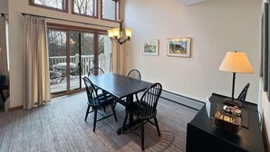 Een eetgedeelte met een tafel en stoelen, een kroonluchter en een uitzicht door grote ramen op een terras.