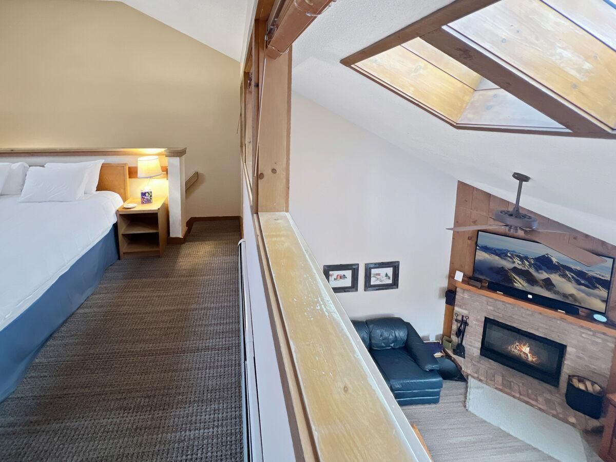 A high-ceilinged room with a bed, a small seating area, a fireplace, and a television.