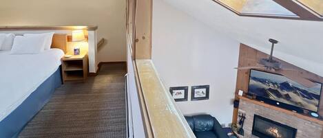 A high-ceilinged room with a bed, a small seating area, a fireplace, and a television.