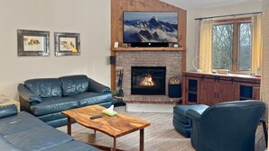 Een woonkamer met een open haard, leren banken, een salontafel en een televisie boven de haard.