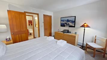 A neatly arranged bedroom with a large bed, wooden wardrobe, a desk with a lamp, and a chair.