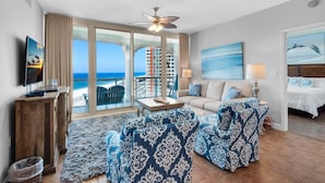 A hotel room with a large balcony, a sofa, a coffee table, and a TV. - Portofino Island Resort 1-1402 (Pensacola Beach)