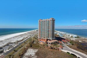 A high-rise hotel with a beach view, multiple balconies, and a parking area. - Portofino Island Resort 1-1402 (Pensacola Beach)