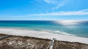 Une plage avec une promenade en bois menant au rivage, un ciel dégagé et une mer calme.