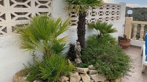 A terrace with a white wall, palm plants, a rock wall, and a statue. - Mountain villa + sea view. Privacy, tranquillity. Near Javéa, Moraira and Dénia (VC)