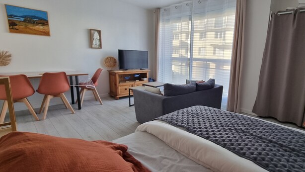 A hotel room with a bed, a sofa, a desk with a chair, a television, and large windows with curtains. - Beautiful renovated apartment in the heart of Concarneau - Private parking - WIFI (Concarneau)