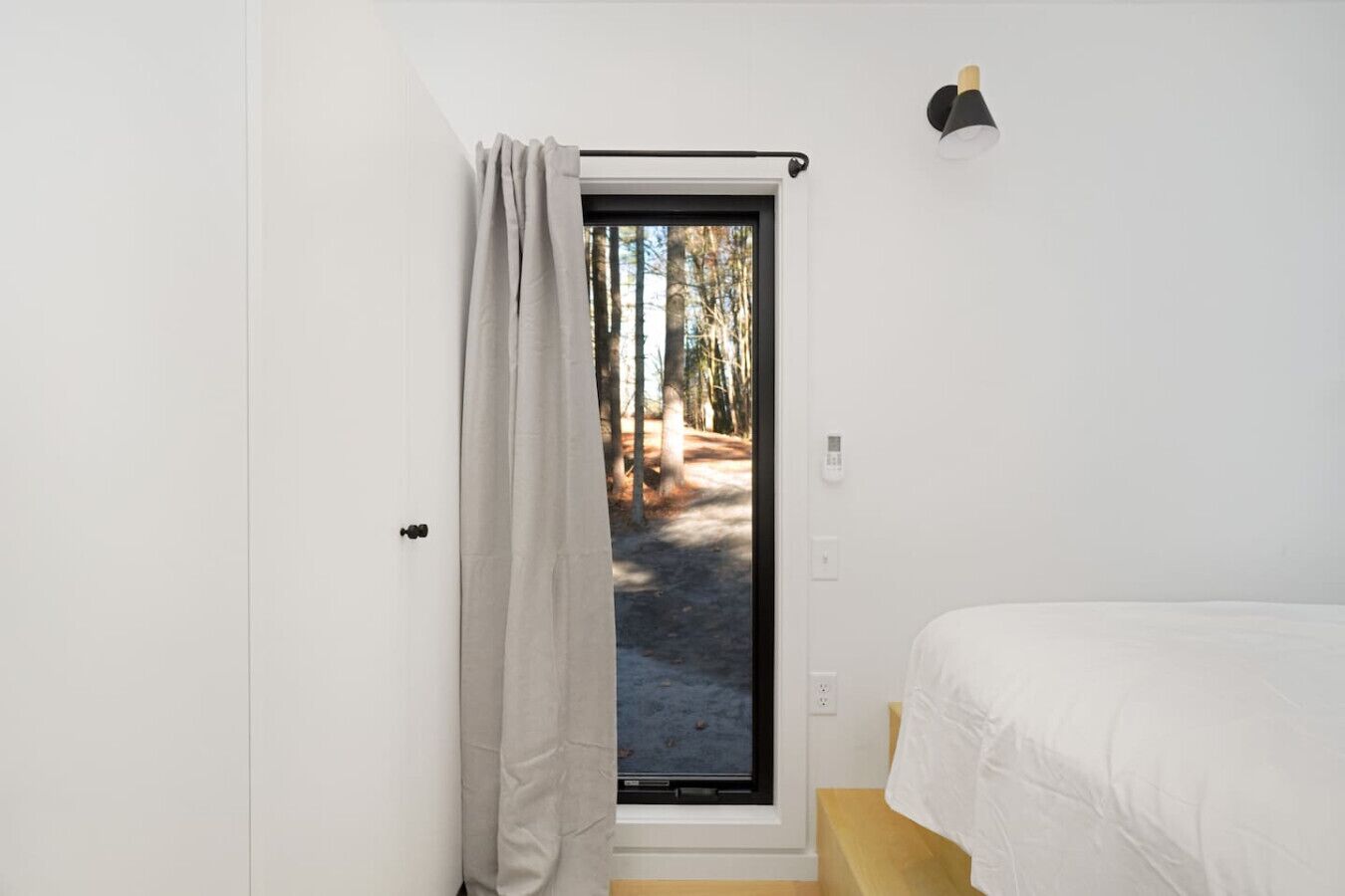 Une chambre avec un lit, une porte donnant sur un espace extérieur et un luminaire fixé au mur.