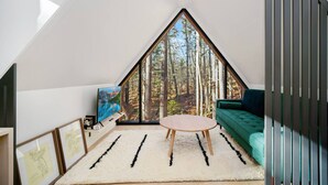 Un dormitori loft modern amb una gran finestra triangular, un sofà verd, una taula rodona i obra emmarcada a la paret.
