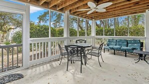 A covered outdoor patio with a wooden ceiling, a ceiling fan, a round table with chairs, and a blue cushioned sofa. - Sand At The Strand-Pool, Cabana, 1/2 Mile To Shops (North Myrtle Beach)