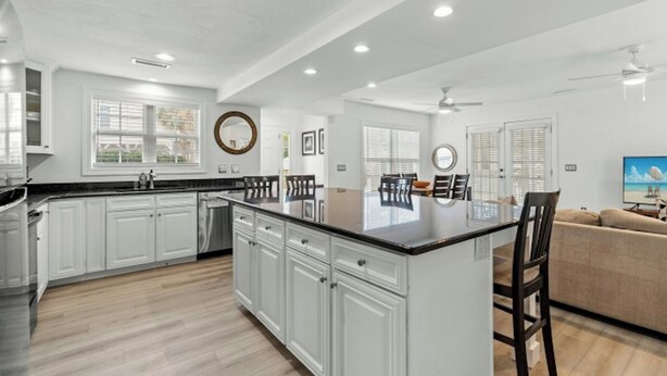 A spacious kitchen with white cabinets, a large island, and a dining area with a glass table and chairs. - Sand At The Strand-Pool, Cabana, 1/2 Mile To Shops (North Myrtle Beach)