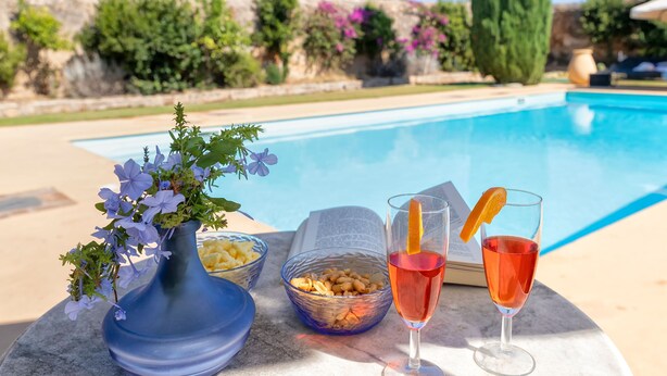 Ein Poolbereich mit einer Blumenvase, Schalen mit Snacks und zwei Getränken auf einem Tisch.