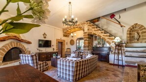 Ein gemütliches Wohnzimmer mit Kamin, einer Sofagarnitur, einem Holztisch und einem steinernen Bogen, der zu einer Treppe führt.