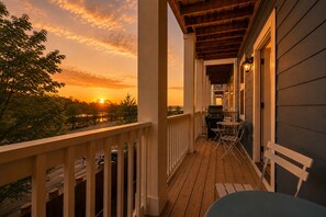 A wooden deck with a railing, a table, and chairs, overlooking a sunset view.
