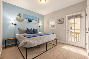 A bedroom with a bed, a nightstand, a wall-mounted lamp, a painting, and a door with a view.