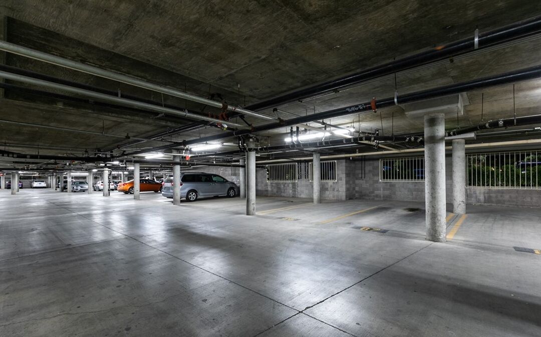 A multi-level underground parking garage with concrete pillars, metal railings, and several parked cars.