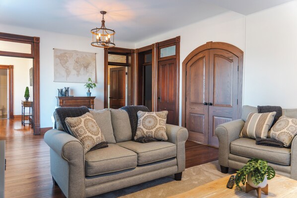 A living room with two sofas, a coffee table, a map on the wall, and wooden doors. - Pony Creek Cottage (North Manchester)