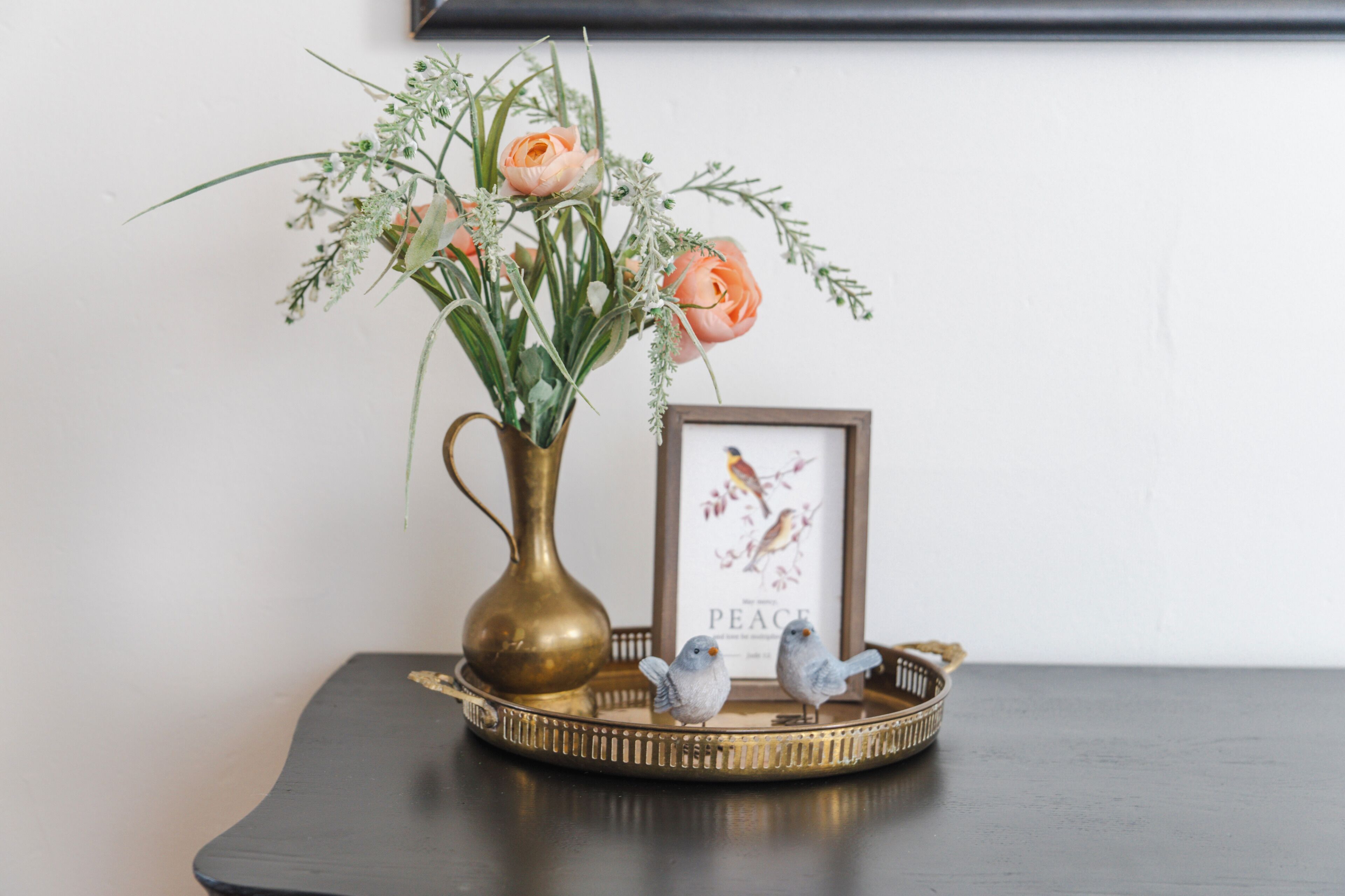 A vase with flowers and a framed picture on a tray with two figurines.