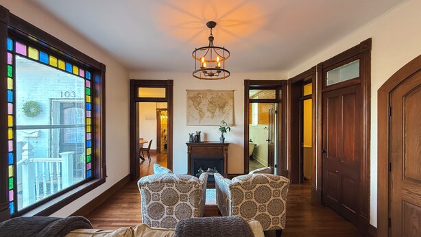 A hallway with a wooden floor, a chandelier, a dining area with a table and chairs, and a large window with colorful panes. - Pony Creek Cottage (North Manchester)