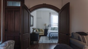 A bedroom with a wooden door, a bedside table, a lamp, a bed with pillows, and a window with curtains. - Pony Creek Cottage (North Manchester)