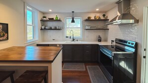 A modern kitchen with a central island, dark cabinetry, a stainless steel stove, and pendant lighting. - Pony Creek Cottage (North Manchester)