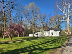 A white house with a black roof, surrounded by trees and a grassy lawn. - Pony Creek Cottage (North Manchester)