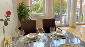 Un comedor con una mesa dispuesta para dos, ventanas amplias con cortinas y vistas a la ciudad.