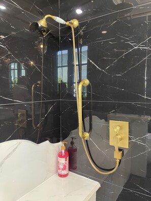 Une salle de bain avec un mur en marbre noir, une pomme de douche dorée et un lavabo blanc.