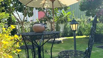 Um pátio externo com mesa, cadeiras, um grande guarda-sol, um vaso de planta e um poste de luz.