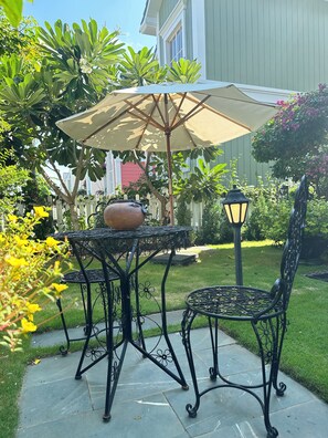 Une terrasse extérieure avec une table et des chaises, un grand parasol, une plante en pot et un lampadaire.