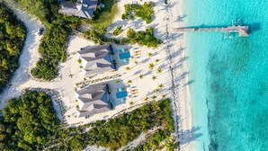 Luchtbeeld van een resort met meerdere bungalowgebouwen, een strand en een steiger die zich uitstrekt in de turquoise zee.