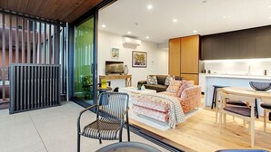 A modern living room with a sofa, a dining table, and a kitchen area. - Gorgeous Home with Catalina Bay Views and Carpark (Auckland West)