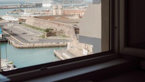 Blick aus einem Fenster auf einen Hafen mit Schiffen und einem Kreuzfahrtschiff, ein Balkon und zwei Tassen auf dem Fensterbrett.